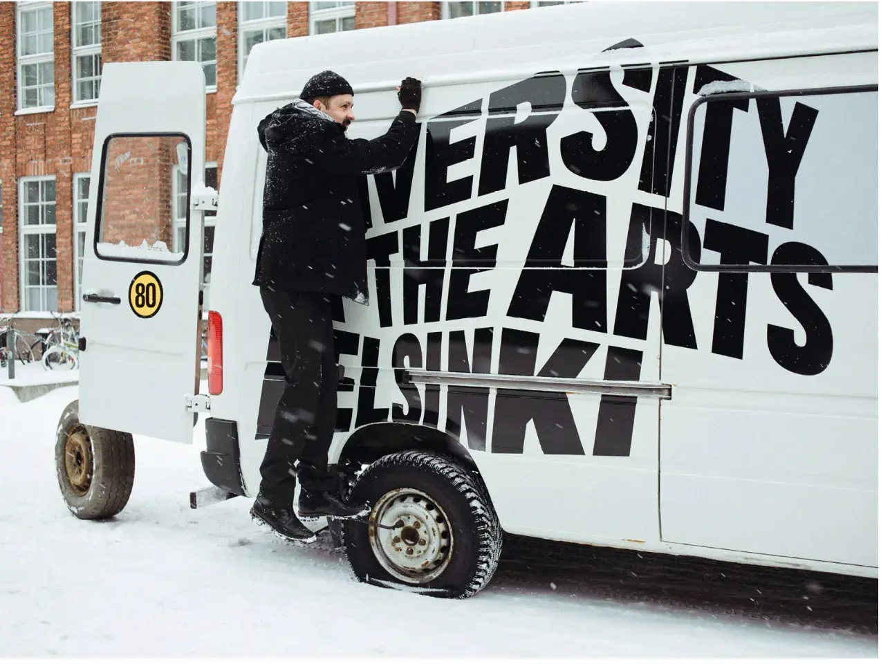 A man applies “University of the Arts Helsinki” to a van in the snow.